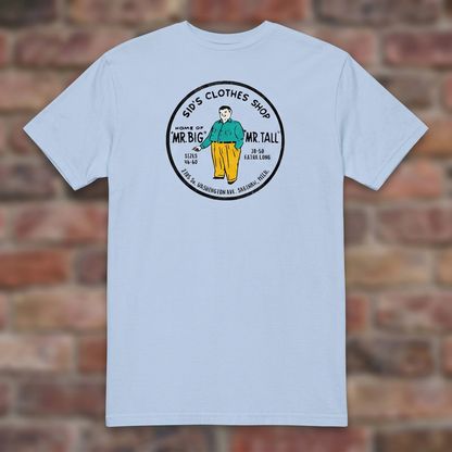 Sid's Clothing Shop Saginaw T-shirt in Light Blue, flat lay on warm brick background