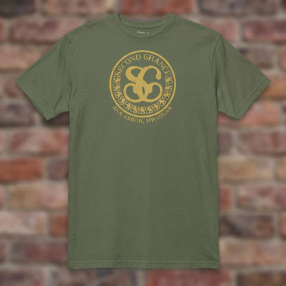 Second Chance Military Green T-shirt flat lay on brick background