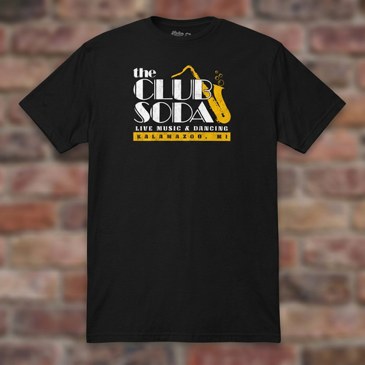 The Club Soda Kalamazoo T-shirt in Black on a weathered brick background
