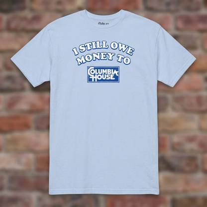 I Still Owe Money To Columbia House Light Blue T-shirt flat lay on brick background