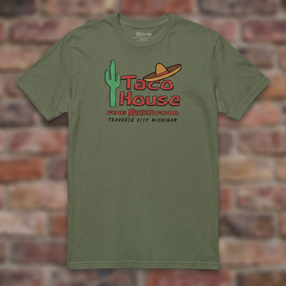 Taco House Traverse City Military Green T-shirt flat lay on brick background