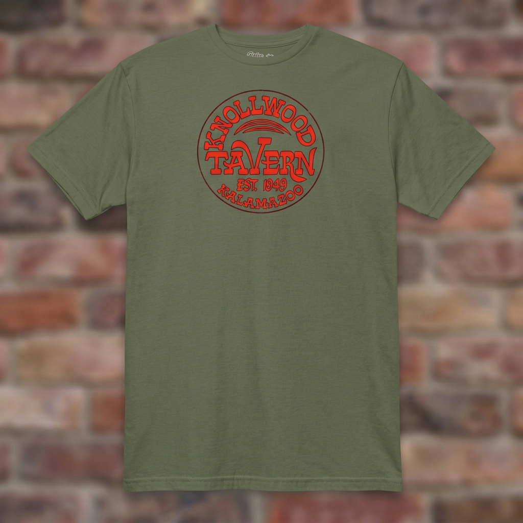 Military Green Knollwood Tavern Kalamazoo T-shirt flat-lay against weathered brick