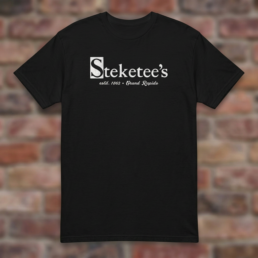 Steketee's Black T-shirt flat lay on brick background