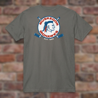 Charcoal Muskegon Mohawks T-shirt laid flat against a weathered brick background