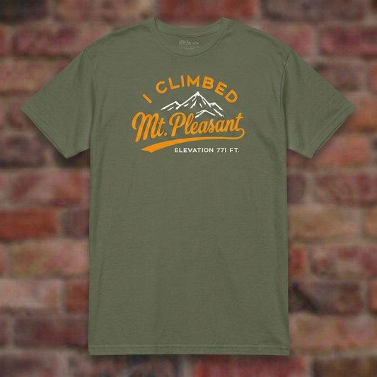 I Climbed Mt Pleasant Military Green T-shirt flat lay on soft brick background